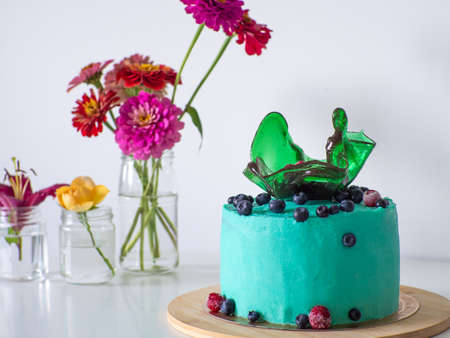 Green blueberry cake with a caramel vase on white background. Birthday cake with cream cheese frosting. green bright cake on the wooden stand with berries decoration. white background with flowers.の写真素材