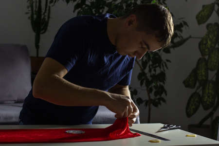 Hands of experienced worker in the handmade industry, performing cutting tasks on red fabric, on a...
