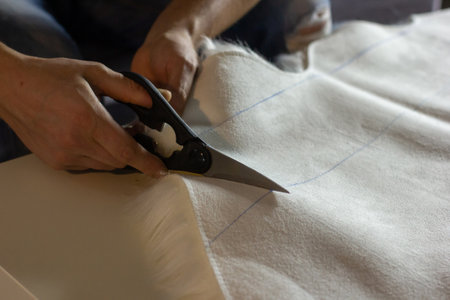 Hands of experienced worker in the handmade industry, performing cutting tasks on white fabric, on a...