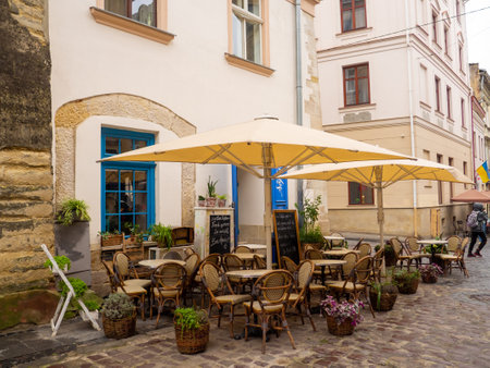 Lviv, Ukraine- July, 2022: Cozy outdoor cafe in the old town of Lviv. Summer cafe with umbrellas in the narrow old street. Vintage tables on paved street among flower pots.のeditorial素材