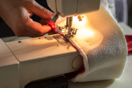 Hands of experienced worker in the handmade industry, sewing red and white fabric on a sewing...