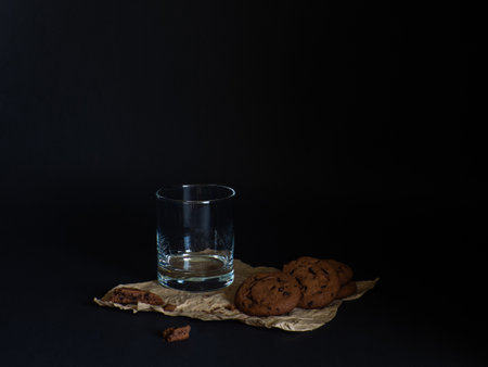 Cookies made from cocoa and with pieces of chocolate inside and empty glass on a baking paper on a black background. copy spaceの写真素材