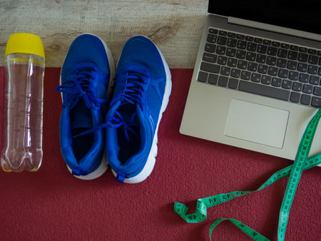 online fitness. Sneakers, laptop, water bottle and measuring tape on a red yoga mat background, workout online. Sports equipment at home. The concept of a healthy lifestyle, training and being fit.の写真素材
