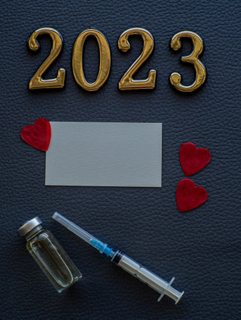 2023, medicine and Vaccination concept. Close up view photo of 2023 and place for text on dark background. Christmas medical card with paper red hearts, syringe, vaccine bottle and copy space.の写真素材
