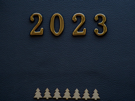 2023 on the dark background. 2023 gold figures lie near small wooden fir trees on the dark cardboard. Christmas and New year card. Copy space for your text.の写真素材
