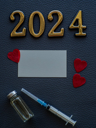 2024, medicine and Vaccination concept. Close up view photo of 2024 and place for text on dark background. Christmas medical card with paper red hearts, syringe, vaccine bottle and copy space.の写真素材