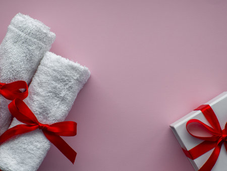 Flat lay with two white towels and gift box wrapped in white paper. Pink paper background with towels tied with a red bows. Valentines day spa, bath, self care and body care concept. Copy space.の写真素材
