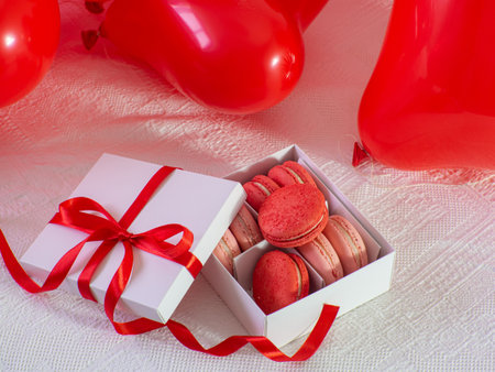 Opened gift box with macaron cookies on the bed. Gift box with sweets lying on white bed with a lot of red heart shape balloons. copyspace. Valentine's day. Buying gifts.の写真素材
