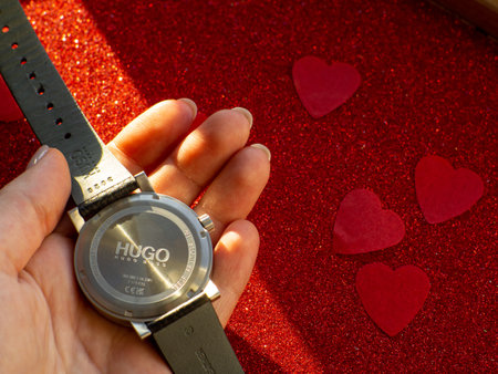 Hugo by Hugo Boss. Black watch is on red heart paper background, reverse side. Greeting card, present. Valentines day holiday concept. Flat lay with an elegant wristwatch and space for text.のeditorial素材