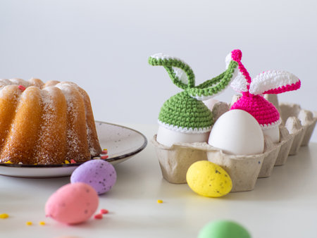Colotful crochet hats with ears for Easter eggs. Crocheted hat with bunny ears. Easter Greeting card. Happy Easter holiday concept with cute handmade eggs with knitted bunny hats and cake.の写真素材