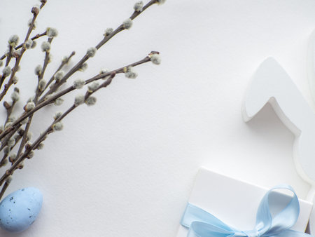 Happy Easter, white concept. Easter decorations on white background with copy space. Easter greating card. Flat lay. Willow twigs, blue egg, white bunny and gift box. Buying gifts for Easter holidaysの写真素材