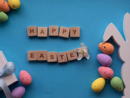 Happy Easter concept. Easter decorations on blue background with copy space. Easter greating card. Flat lay. Colorful eggs, white bunny and gift box. Buying gifts for the Easter holidays.の写真素材