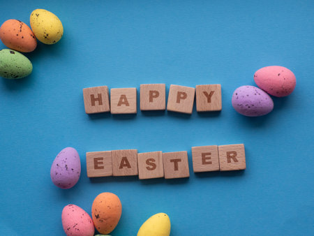 Happy Easter concept. Easter decorations on blue background with copy space. Easter great card. flat lay. Colorful eggs and Happy Easter inscription on wooden cubes. Celebration of spring holidays.の写真素材