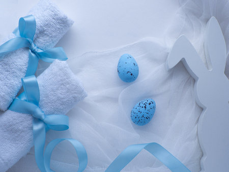 Wellness Easter concept. Set white towels tied with a ribbon in a bow, blue eggs and bunny. White Easter card. Rolled towels in spa salon. Hygiene and spa, relaxation as a gift for holidaysの写真素材