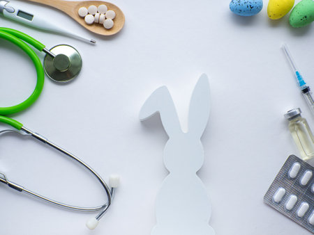 Easter and medicine. Healthy Easter concept. Pills in wooden spoon, thermometer, stethoscope, white bunny and eggs on white background. Dietary supplement for health care. Flat lay.の写真素材