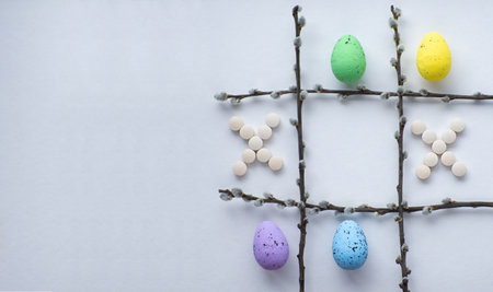 Easter and medicine. Healthy Easter concept. Tic tac toe made of willow twigs, colorful Easter eggs and pills on white background with copy space. Disease on Easter holidays. Flat lay, top view.の写真素材