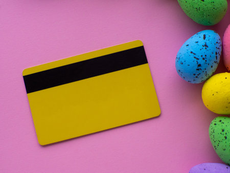 Easter and shopping concept. Ordering Easter gifts. Shopping cart with colorful eggs, credit card on pink background with copy space. Online store. Expensive celebration of the Easter holidays.の写真素材