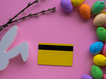 Easter and shopping concept. Ordering Easter gifts. Credit cart with colorful eggs and white bunny on pink background with copy space. Online store. Expensive celebration of the Easter holidays.の写真素材