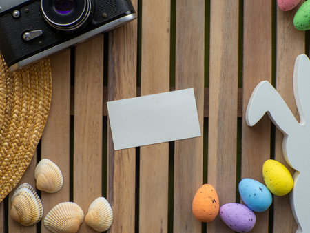 Wooden background with straw hat, photo camera, shells, colorful eggs and white rabbit. Easter card design with copy space. Easter and traveling concept. Rest and trip during holidays.の写真素材