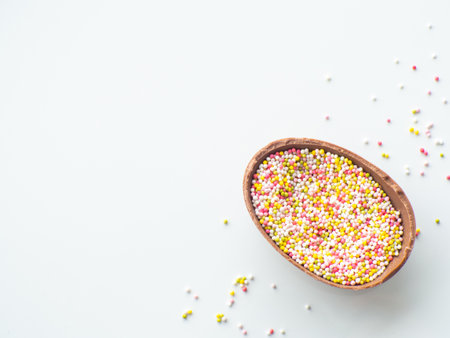 Sweet Easter concept. Chocolate easter egg with sweet sprinkles on white background with copy space. Design for a greeting card for the Easter holiday. Flat lay. Preparation for holiday.の写真素材
