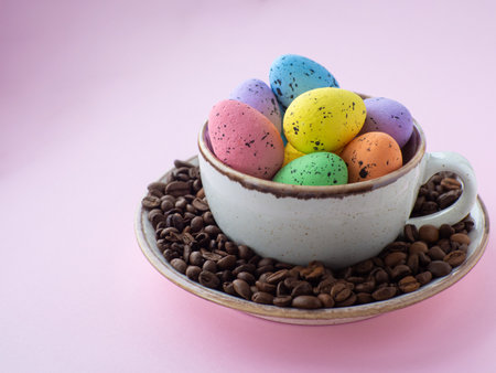 Composition with easter eggs in cup surrounded by coffee roasted beans. Easter coffee concept. Mug full of colorful eggs on a plate with coffee beans on a pink background with copy space.の写真素材