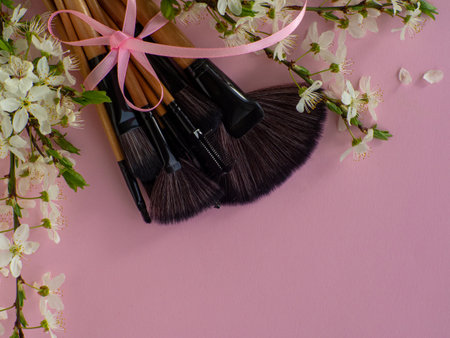 Bouquet of cosmetic brushes tied with a pink ribbon with a bow on pink background with cherry flowers and copy space. Women and Mothers Day gift. Concept of beauty and femininity. Buying gifts online.の写真素材