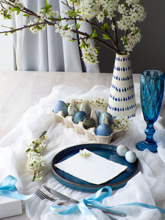 Festive Easter table setting with flowers, painted eggs and gift box on white background. Elegance...