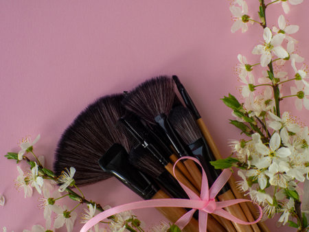 Bouquet of cosmetic brushes tied with a pink ribbon with a bow on pink background with cherry flowers and copy space. Women and Mothers Day gift. Concept of beauty and femininity. Buying gifts online.の写真素材