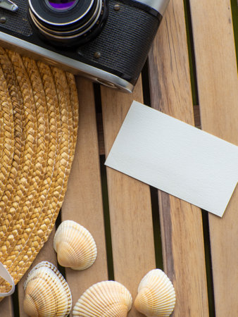 Wooden background with straw hat, photo camera, shells and space for text. Card design with copy...