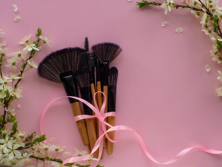 Bouquet of cosmetic brushes tied with a pink ribbon with a bow on pink background with cherry flowers and copy space. Women and Mothers Day gift. Concept of beauty and femininity. Buying gifts online.の写真素材