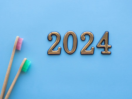 2024 and dental concept. Close up view of photo with 2024 and two wooden colorful toothbrush on blue background with copy space for text. Christmas medical card. Merry Christmas and Happy New Year.の写真素材