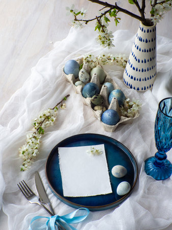 Festive Easter table setting with card, painted eggs and spring flowers on white background. Elegance pastel and blue tablescapes. Easter celebration. Delicate Easter composition. View from above.の写真素材