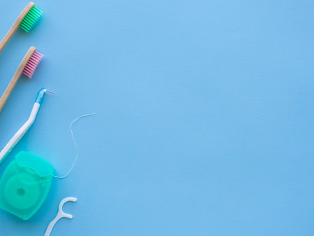 Dental concept background with copy space for text. Close up view of photo with dental floss, floss stick and wooden toothbrush on blue background. Medical card for design.の写真素材