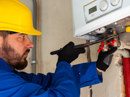 Installing heating and water pipes in apartment. Maintenance jobs for water and heating systems. Concept of plumbing and home renovation. Worker attach the tube to boiler with adjustable pipe wrench.の写真素材