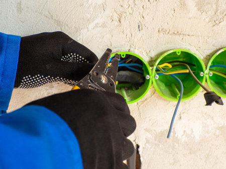 Professional electrician working on home electrical system. Green round plastic backbox for sockets or switches inserted into the drilled holes on wall. New electrical installation, renovation conceptの素材 [FY310211025203]