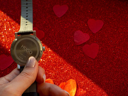 Hugo by Hugo Boss. Black watch is on red heart paper background, reverse side. Greeting card, present. Valentines day holiday concept. Flat lay with a elegant wristwatch and space for text.のeditorial素材