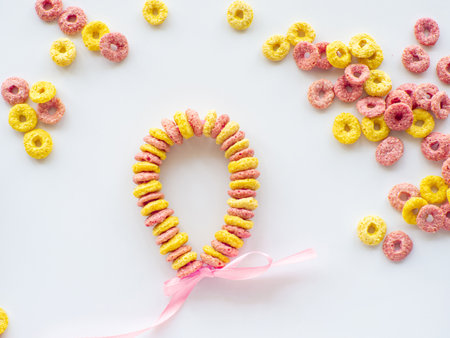 Edible DIY bracelet or necklace for Mothers day. DIY for kids. Bracelet made with froot ring shaped cereal. Making gift with fruit loops for Mothers day. Colored cereals background with copy space.の写真素材