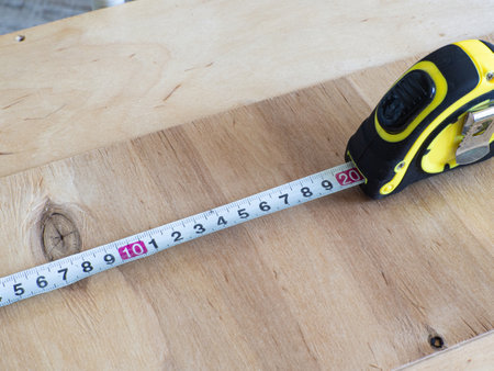 A detailed close-up image showing a yellow tape measure laid flat on a smooth beige wooden background. Ideal for home improvement or construction themes.の写真素材