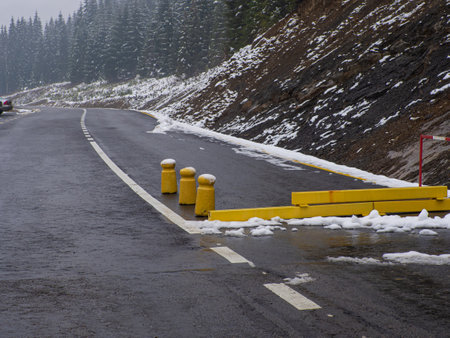 Road closed barrier blocking dangerous snow ice weather covered road with covered trees and icy surface. Yellow barrier on the road of the Bukovel mountain pass in Ukraine - danger of avalanches.の写真素材