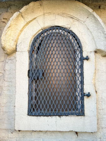 Close up view of closed metal arched window with brick wall, creating a rustic and historic lookの写真素材