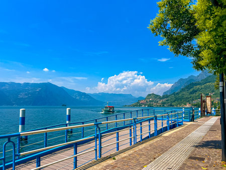 Ferry dock in the town of Sale Marasino on sunny summer day. A small pier along the shore of Lake Iseo, Lombardy, Italy. A passenger ship arrives at the pier on Lake Iseo from Monte Isolaの写真素材
