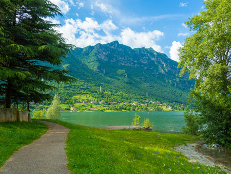 Stunning landscape featuring a calm lake reflecting the cloudy sky. Majestic mountains rise in the distance, framed by lush greenery, creating a tranquil and picturesque scene. Lake Idro, Crone, Italyの写真素材