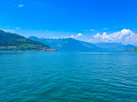 A stunning landscape featuring a calm Iseo lake reflecting the blue sky, Italy. Majestic mountains rise in the distance, framed by lush greenery, creating a tranquil and picturesque scene.の写真素材