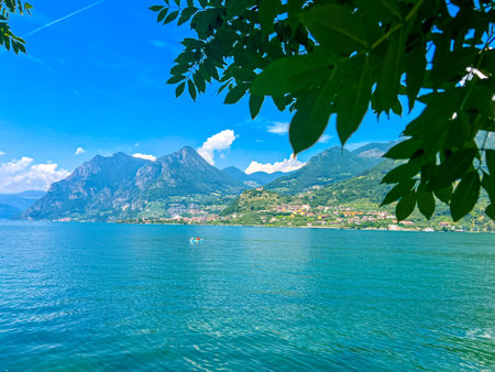 A stunning landscape featuring a calm Iseo lake reflecting the blue sky, Italy. Majestic mountains rise in the distance, framed by lush greenery, creating a tranquil and picturesque scene.の写真素材