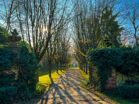 A charming entrance to a picturesque english country garden, framed by tall, lush trees. The serene pathway invites visitors into a tranquil floral haven, showcasing natures beauty.の写真素材