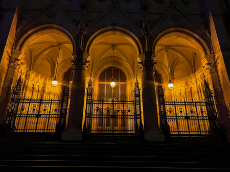 A mesmerizing nighttime view of budapests gothic architecture, highlighting the illuminated arched doors of the parliament building, showcasing intricate details in a captivating atmosphere.の写真素材