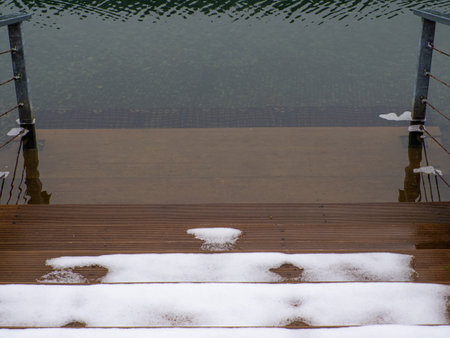A staircase covered in snow. Snowy wooden Steps Leading to lake. The image has a peaceful and serene mood.の写真素材