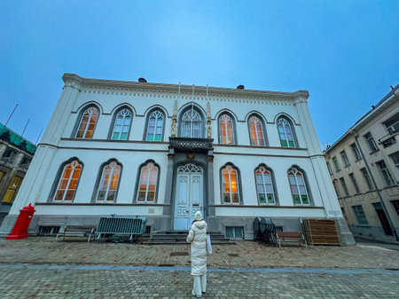 An elegant white gothic-style building facade in Ghent, showcasing intricate architectural details. A woman stands outside, adding a touch of life to this picturesque scene.の写真素材
