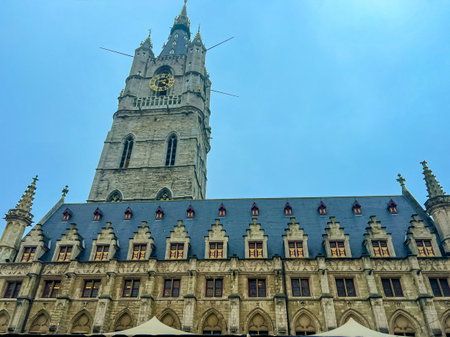 A breathtaking view of the iconic belfry tower and the majestic cathedral in historic Ghent, set against a backdrop of vibrant blue skies, showcasing the beauty of belgian architecture.の写真素材