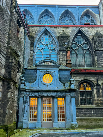 Capture the stunning exterior of an ancient Ghent church, showcasing intricate gothic details illuminated by a beautiful blue light. A captivating blend of history and artistry.の写真素材